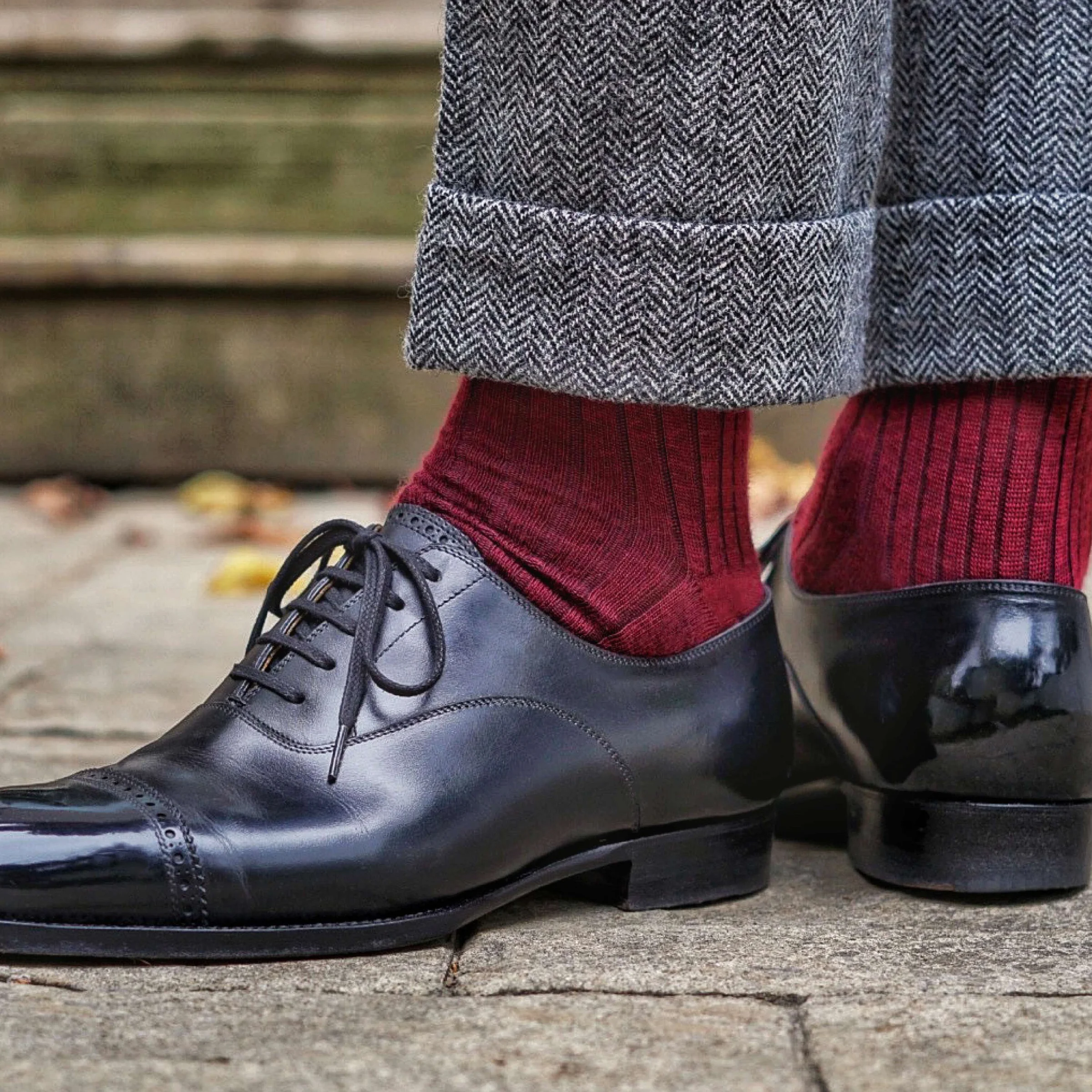 man standing outside wearing burgundy merino wool ribbed dress socks with herringbone slacks and black oxfords
